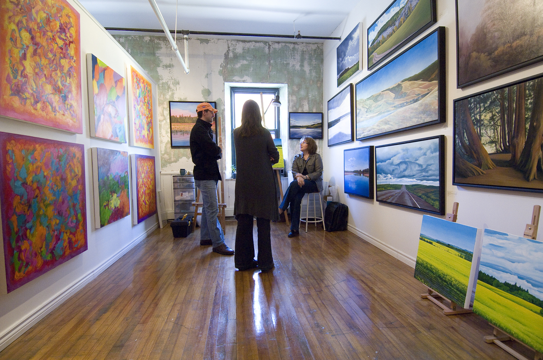 Artist showing their art to two visitors in a bright studio